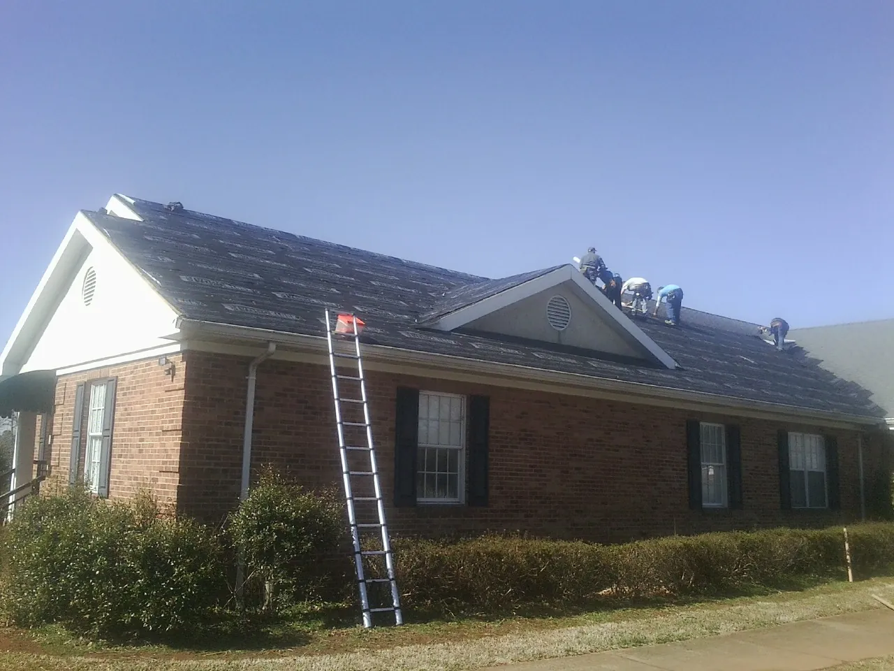 Crew tearing shingles off a brick ranch roof with a ladder set — Metal Roof Repair work by our crew in Seaton