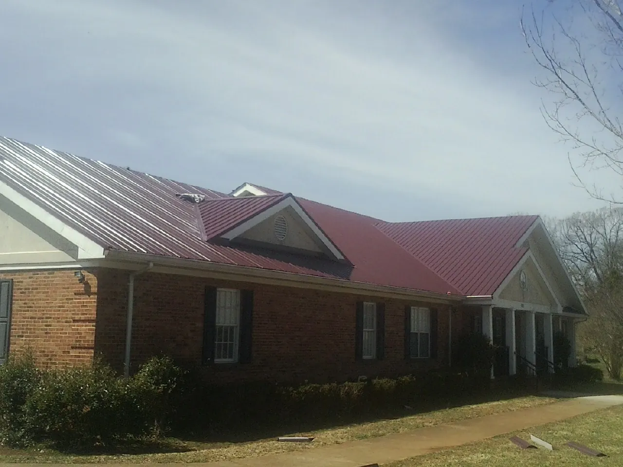 Red metal roof with gabled entries on a long brick building, from a Hail Damage Roof Repair job in Seaton