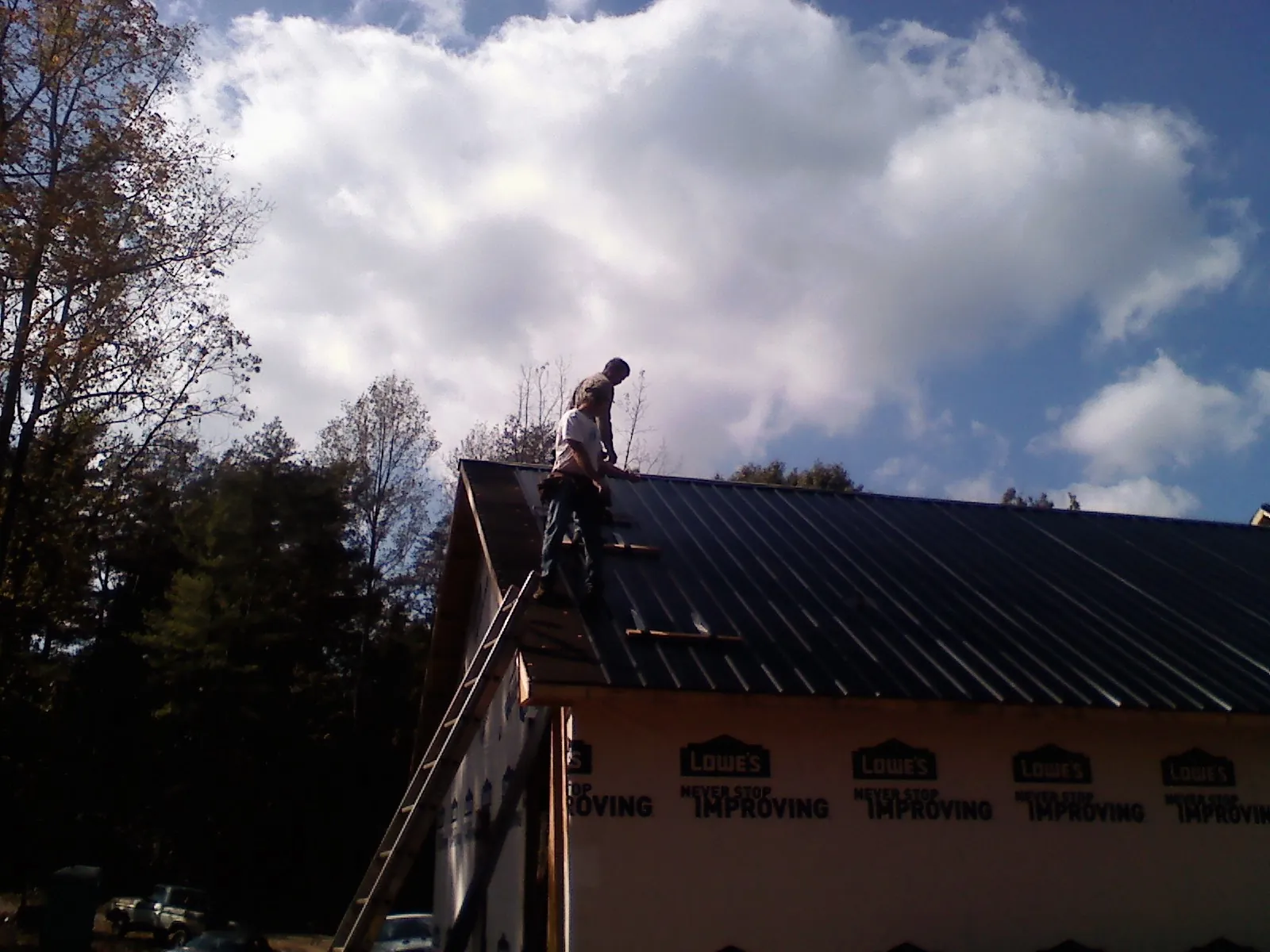 Roofer fastening dark metal panels high against a cloudy sky, from a Roof Inspection job in Seaton